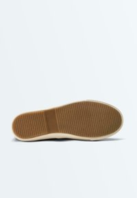 Semelle en caoutchouc marron avec une surface texturée antidérapante et une semelle intermédiaire beige, vue de dessous sur un fond blanc.