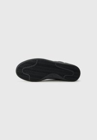 Semelle de chaussure en caoutchouc noir avec un motif en vagues. Présente une finition lisse et des bords arrondis, étiquetée avec la taille 37.