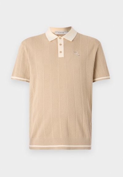 Šviesiai rudas megztas polo marškinėliai su ryškia struktūra, trijų mygtukų užsegimu, kontrastinga kreminės spalvos apykakle ir kraštais, puikuojasi mažuoju logotipu ant krūtinės.