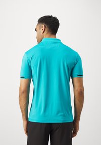 Turkizna polo majica s kratkimi rokavi in ovratnikom. Ima teksturirano blago in črne poudarkovne črte na rokavih. Prikazan zadnji pogled.