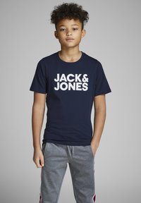 Tirač z mornarsko modrega bombaža s širokim belim logotipom "JACK & JONES". Usklajen s sivimi trenirkami, ki imajo zanko in stranske črte.