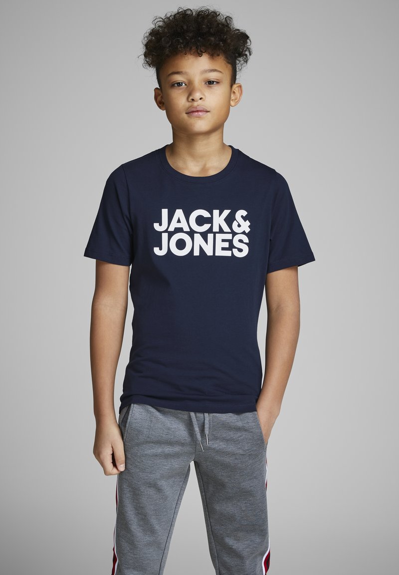 Tirač z mornarsko modrega bombaža s širokim belim logotipom "JACK & JONES". Usklajen s sivimi trenirkami, ki imajo zanko in stranske črte.