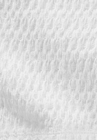 Tissu blanc texturé avec un motif ondulé, présentant un fin canalé et une apparence douce, idéal pour des vêtements légers ou des textiles d'intérieur.