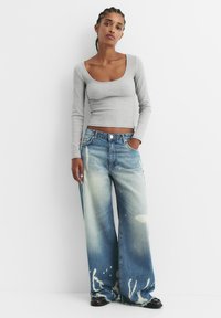 Grijze lange mouw top met een ronde hals gecombineerd met wijde blauwe denim jeans met een vervaagde was en bleekvlekken.