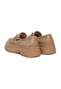 Tlusté béžové loafery s robustními drsnými podrážkami, síťovinovými bočními panely a stříbrnými řetízkovými akcenty na bílém pozadí.