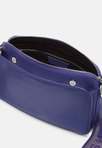 Borsa a tracolla compatta in pelle viola con tasca anteriore con chiusura a scatto, zip superiore e tracolla in tessuto regolabile con hardware in metallo.