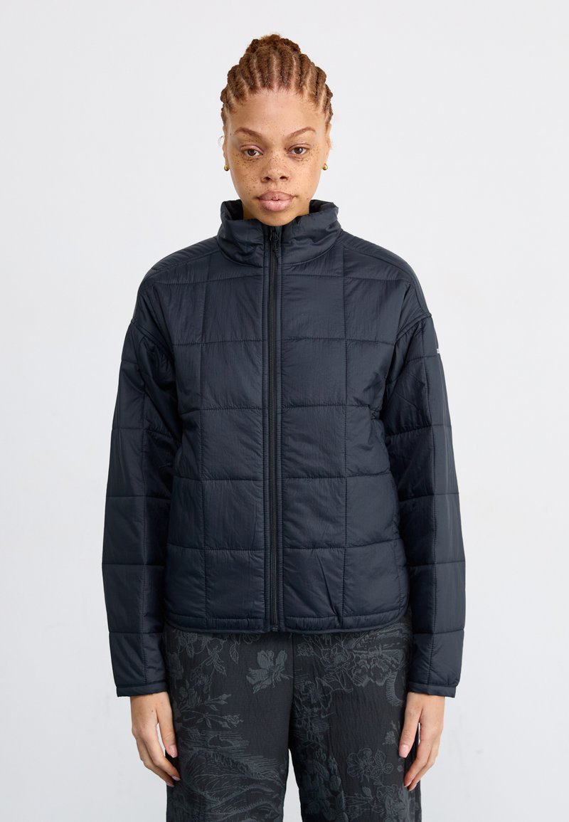 Veste matelassée noire avec un col haut, dotée d'un design matelassé, fermeture éclair frontale intégrale et coupe légèrement ample. Convient pour les superpositions.