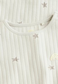 Lys grå bomuldsbeklædning med lodrette striber, der har svage stjerner og en broderet regnbue. Blød tekstur med rund halsudskæring.