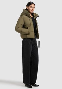 Olive green puffer jacket with a hood, zippered front, and two side pockets. Paired with black wide-leg jeans and heeled black boots.