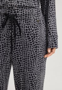Ingezoomd uitzicht op grijze loungekleding met een zwart, gestructureerd ruitpatroon. De top heeft knoopsluiting en losse manchetten; de broek heeft een trekkoord.