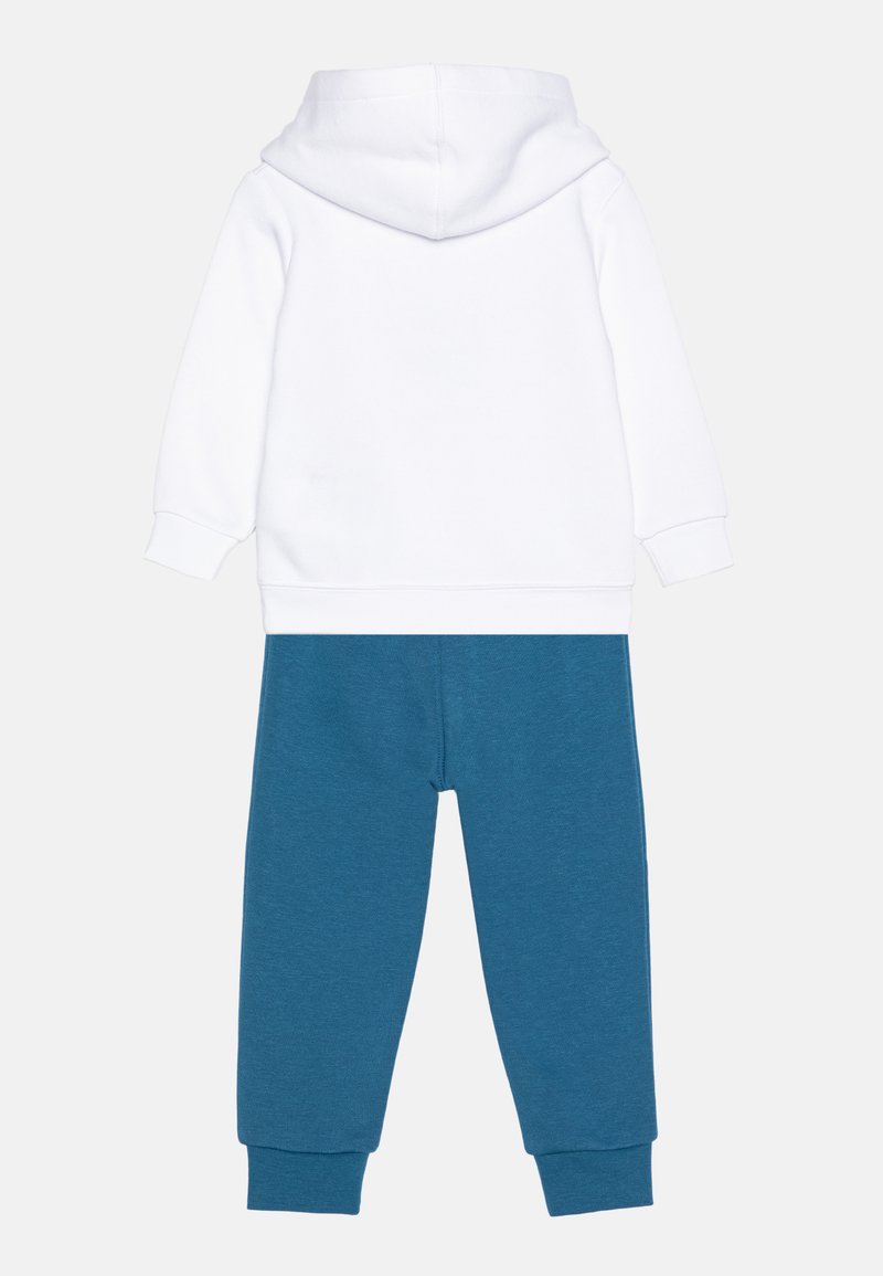 Sudadera con capucha blanca de mangas largas y bolsillo canguro, combinada con pantalones de chándal azules con una textura suave y puños acanalados.