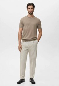 Camisa de punto beige de manga corta combinada con pantalones beige claros, ajustados, de textura suave, y botas de tobillo de cuero negro para un look cohesivo.