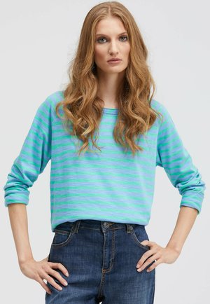Long-sleeve striped shirt in light blue and green. Soft fabric, relaxed fit, crew neckline, and rolled cuffs. Paired with dark denim jeans.