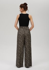 Svart ärmlös topp som kombineras med högmidjade byxor med vida ben, prydda med ett beige leopardmönster på svart botten.