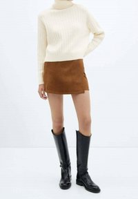 Maglione a collo alto a coste color crema, minigonna in suede marrone e stivali in pelle nera fino al ginocchio, caratterizzati da una texture liscia e un design semplice.