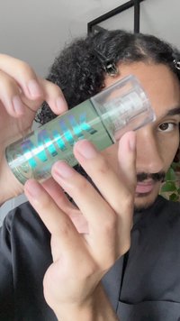 Clear green spray bottle with a transparent cap, featuring bold holographic text reading "MILK." Smooth texture and minimalist design.
