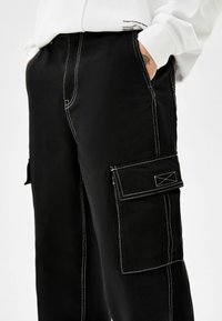 Svart cargobyxor gjorda av hållbart tyg med vit kontrastsöm, med sidofickor och en avslappnad passform för funktionalitet.