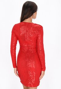 Rochie roșie, cu mâneci lungi, acoperită cu paiete, cu o siluetă ajustată. Suprafața texturată prezintă dungi verticale de paiete, evidențiind forma corpului.