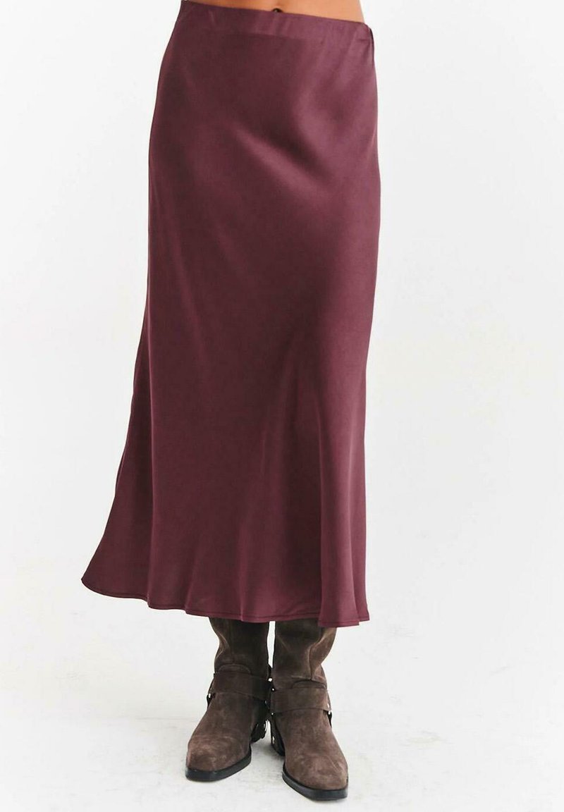 Dlouhá hladká burgundská sukně v kombinaci s hnědými semišovými botami na střední lýtka se sponami a nízkými podpatky na jednobarevném bílém pozadí.