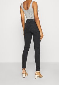 Top sin mangas gris combinado con jeans skinny negros de cintura alta, con una textura suave y puños enrollados, complementado con sandalias de tacón bloque.