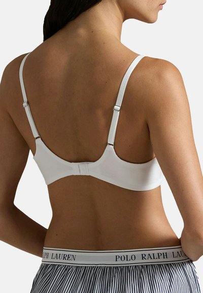 Reggiseno bianco a coste con spalline regolabili, chiusura a gancio sul retro, indossato con pantaloni da pigiama a righe con una vita personalizzata.