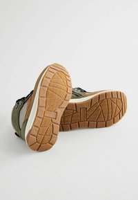 Baskets avec une tige verte et marron en mélange de matériaux, semelle en gomme texturée avec un motif en zigzag et un col rembourré.
