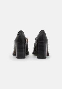 Scarpe con tacco alto in pelle nera con un tacco testurizzato e rigido. Presentano una punta affusolata e una finitura liscia, adatte per abbigliamento formale.