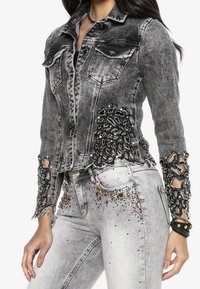 Haalean musta farkkutakki, jossa on yksityiskohtaiset mustat pitsikoristeet ja somisteet hihoissa. Takissa on kaksi rintataskua ja hopeanväriset metalliosat.