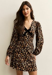 Robe en imprimé léopard avec de longues manches bouffantes, un décolleté en V profond et un accent en nœud en velours à la taille, fabriquée en tissu léger.