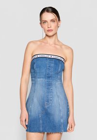 Denim strapless dress with a fitted bodice and frayed hem. Features a branded band at the top. Light blue color with visible seams.