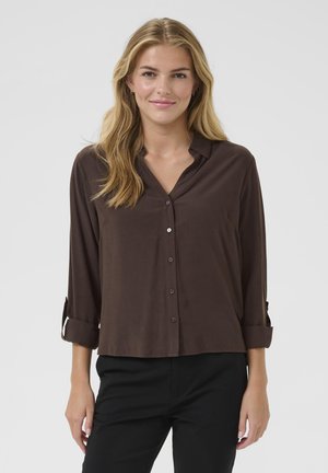 Brown button-up shirt made of smooth fabric, featuring a collar, long sleeves rolled to the elbows, and a relaxed fit.