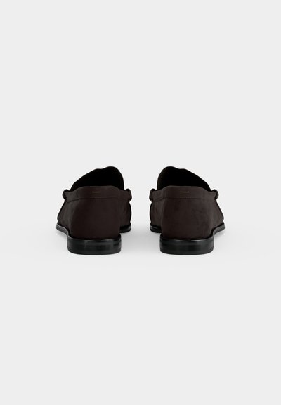 Paire de chaussures habillées en daim marron foncé vue de dos sur un fond clair uni.