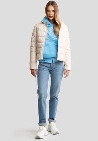 Puffjakke i creme, parret med en blå hoodie og lyseblå jeans. Sneakers er hvide med grå accenter. Subtle quiltet tekstur.