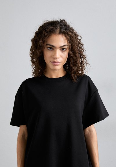 Fekete, nagyméretű póló, puha anyagból, kerek nyakkivágással és rövid ujjakkal. Egyszerű, letisztult vonalai vannak, látható minták nélkül.
