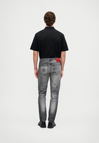 Crna kratka majica s kragnom, uparena s uskim sivim trapericama koje imaju crveni oznaku na stražnjem remenu. Crne cipele.