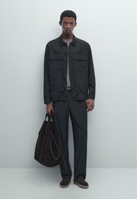 Giacca nera a bottoni con due tasche sul petto, abbinata a pantaloni coordinati. Tieni una borsa in tessuto morbido scuro e indossa scarpe scure.