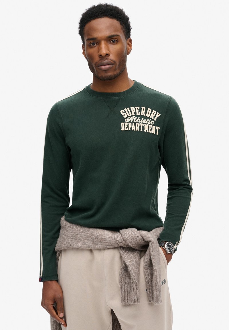 Mørkegrøn langærmet skjorte med "SUPERDRY Athletic Department" i cremefarvet tekst. Har hvide sidelister, blød tekstur og en rund halsudskæring.