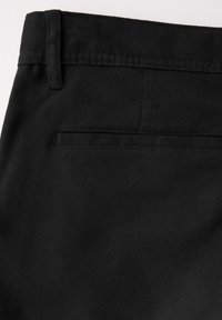 Svarta bomullsgrejer med en texturerad yta, med en bakficka och bältesömmar, fokus på släta sömmar och minimalistisk design.