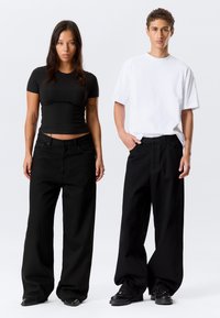 Jean noir taille haute à jambes larges associé à un t-shirt noir ajusté et un t-shirt blanc décontracté ; les deux présentent un design minimaliste.