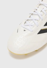 Witte voetbalschoenen met een glanzende afwerking, voorzien van reliëfpatronen, zwarte accenten en gele noppen. De veters zijn wit met geperforeerde secties.