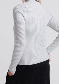 Jasnoszara, prążkowana bluzka z długim rękawem i wysokim dekoltem; dopasowany krój; teksturowany materiał; noszona na czarnej spódnicy.