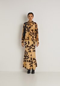 Animal print lange mouw top en bijpassende rok in beige met zwarte accenten; gladde textuur en een losse pasvorm; gecombineerd met zwarte enkellaarsjes.