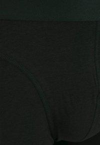 Schwarze Baumwollmischung-Unterwäsche, die eine glatte Textur, einen elastischen Bund und eine genähte Detailverarbeitung entlang der Kanten zeigt.