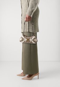 Mała torebka w odcieniach beżu i brązu, wykonana z teksturowanej tkaniny, z złotym okuciem i dekoracyjnymi białymi paskami. Stylizowana z oversize'owym swetrem i szerokimi spodniami.