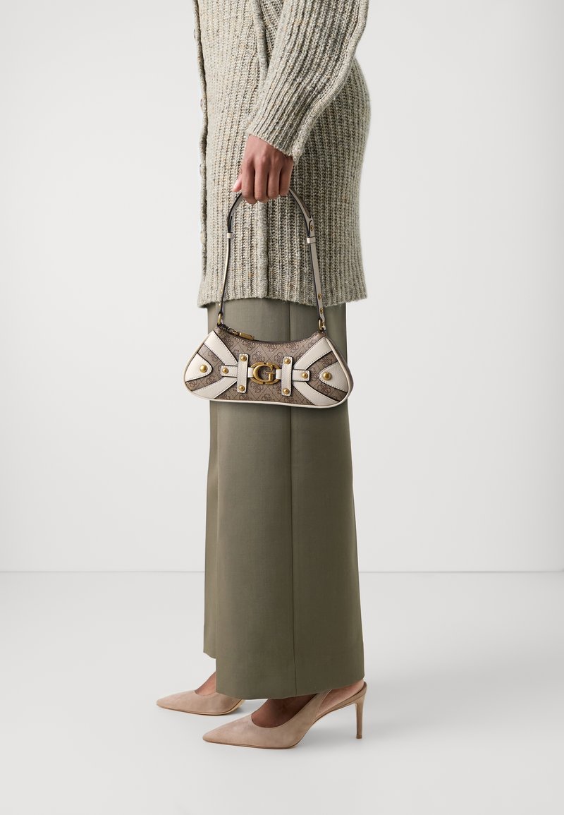 Mała torebka w odcieniach beżu i brązu, wykonana z teksturowanej tkaniny, z złotym okuciem i dekoracyjnymi białymi paskami. Stylizowana z oversize'owym swetrem i szerokimi spodniami.