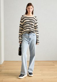 Maglione a righe in crema e nero, dalla vestibilità comoda; abbinato a jeans azzurri chiari, con una cintura nera e una piccola borsa nera.