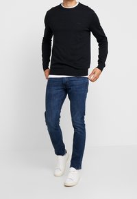 Black sweater with a round neckline and long sleeves, paired with blue jeans and white sneakers. Simple, casual design.