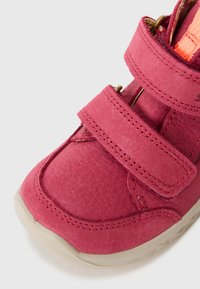 Różowe buty na rzepy z teksturowanej skóry, z zaokrąglonym czubkiem i beżową gumową podeszwą. Podwójne rzepy ułatwiają szybkie zapinanie.