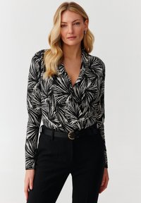 Top de manga larga en blanco y negro con un patrón de hojas, con un escote drapeado y un ajuste ceñido, combinado con pantalones negros de cintura alta.