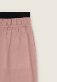 Joggers de color rosa claro con una cinturilla elástica negra, textura suave y detalle fruncido en la cintura, que muestran un ajuste relajado.